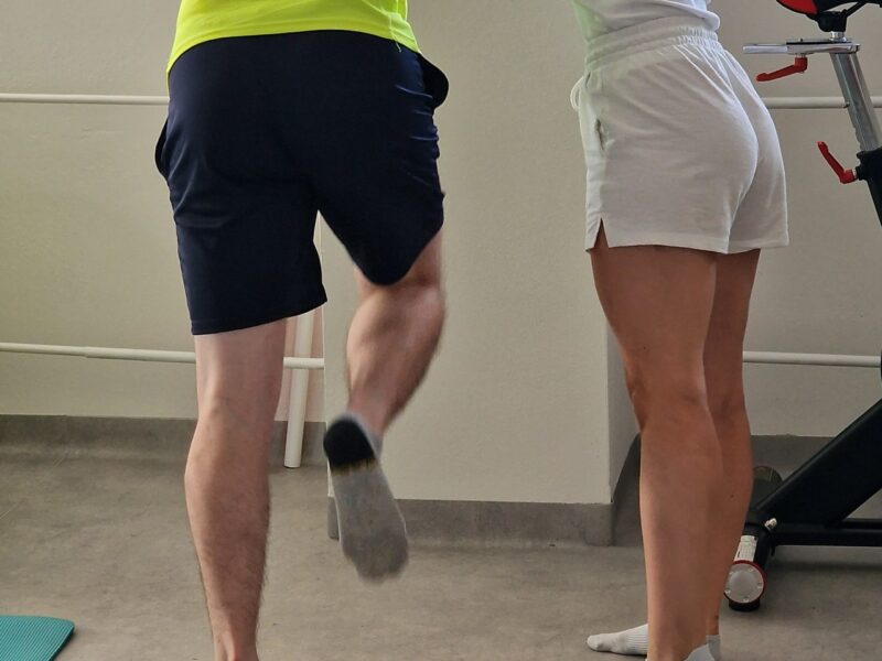 Fyzioterapeutka koriguje postavenie trupu a ramenného pletenca pri silovom cvičení na jednej nohe s oporou o stenu počas skupinového cvičenia FyzioSila v Košiciach.