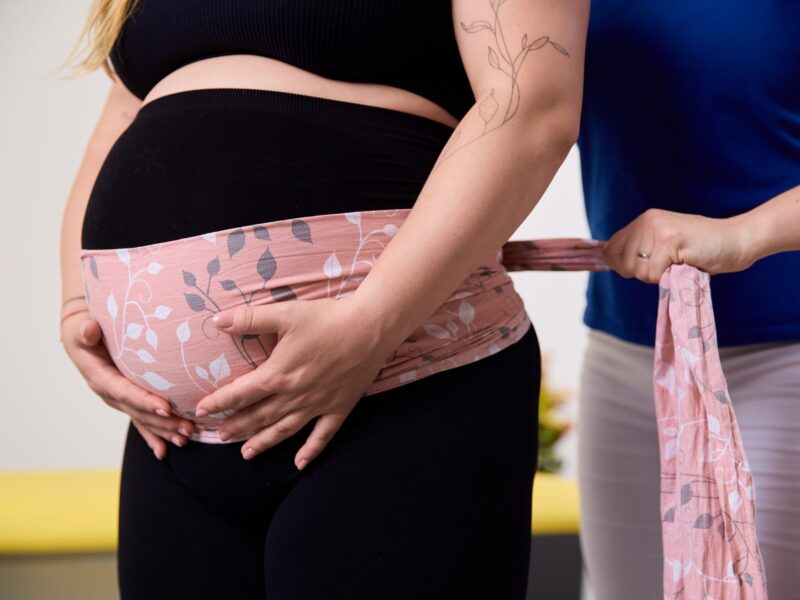 Fyzioterapeutka spevňuje tehotenské brucho podpornou šatkou po tehotenskej masáži v Košiciach.