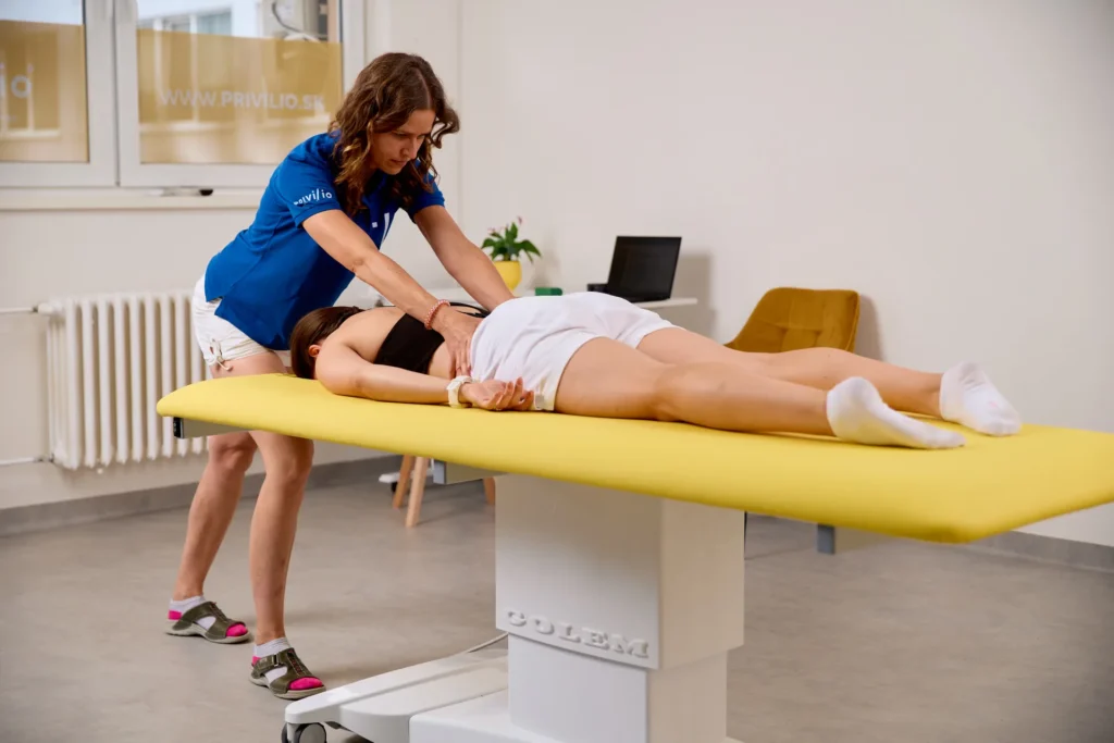Fyzioterapeutka uvoľňuje manuálnou technikou driekovú oblasť chrbta klientke ležiacej na terapeutickom stole.